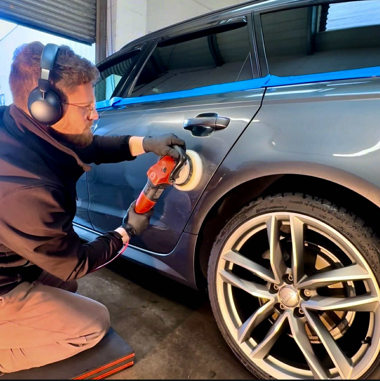 Machine polishing the rear quarter panel of a grey Audi estate